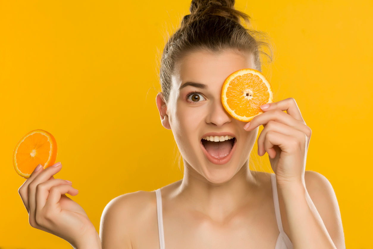Junge schöne Frau hält eine Orangenscheibe vor ihr Auge auf gelbem Hintergrund